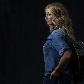 Woman in denim shirt with guitar on her back